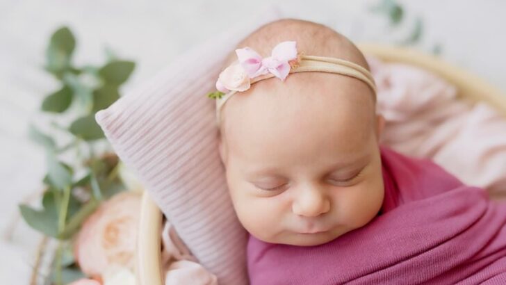 Bebê com faixa na cabeça dormindo em cesto enrolada em lençol rosa