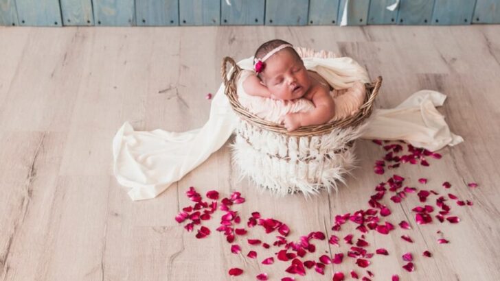Bebê com faixa na cabeça dormindo em cesto perto de pétalas de flores