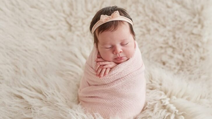 Bebê com faixa na cabeça enrolada em lençol rosa com fundo fofo