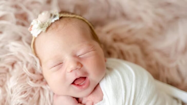 Bebê de boca aberta e faixa na cabeça deitado em fundo fofo