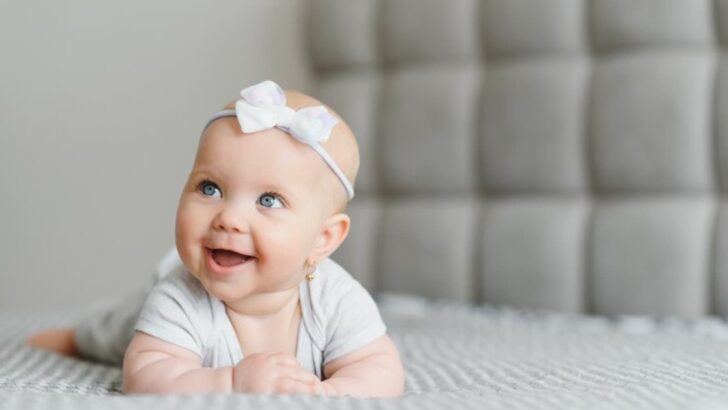 Bebê de tiara deitada de bruços em cama sorrindo