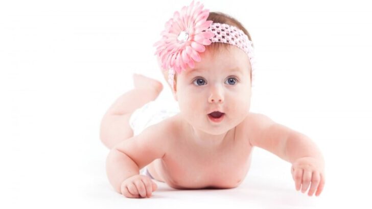 Bebê de tiara rosa deitada de bruços em fundo branco