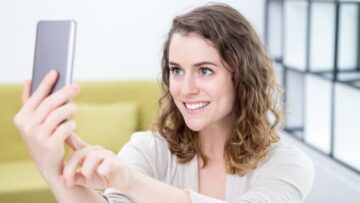 Mulher sorrindo olhando para o celular na mão