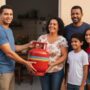Família brasileira recebendo um botijão de gás grátis em casa por um agente do programa Gás do Povo, pessoas sorrindo e aliviadas