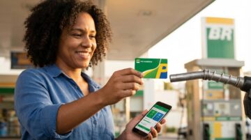 Pessoa brasileira segurando cartão Petrobras Premmia em posto de gasolina enquanto consulta o celular sobre economia
