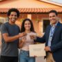 Família brasileira sorrindo em frente à casa nova segurando chaves e documentos do programa Minha Casa Minha Vida